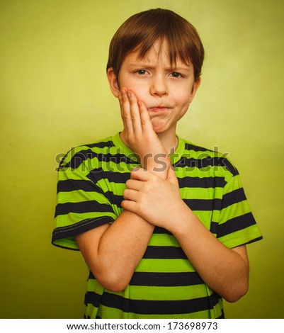 young boy child toothache pain in mouth, dental pain, holding his cheek on a green background gray large