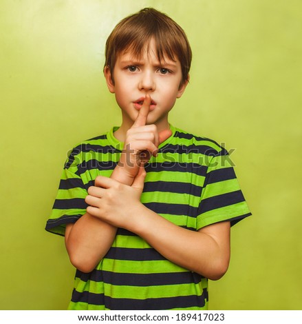 young boy kid shows sign hand gesture finger to lips mouth shh silence means quiet on green background