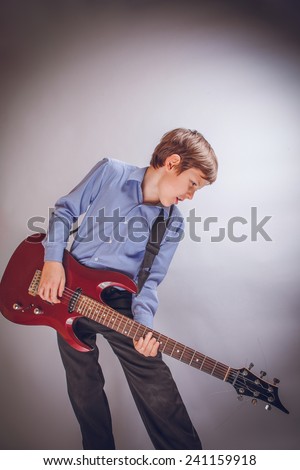 teenager boy of 10 years of European appearance playing guitar on a gray background cross process
