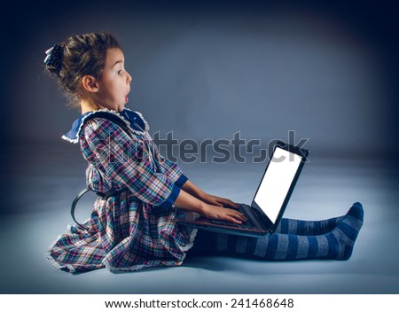 Teen girl sitting on the floor playing laptop surprised on a gray background cross process