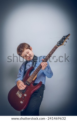 Teen boy playing  guitar on a  gray  background cross process