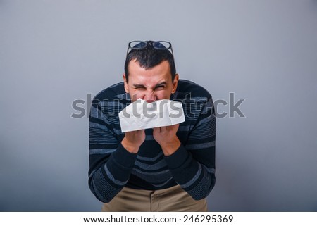 European-looking male of about thirty brunet blowing his nose into a handkerchief on a gray background, runny nose