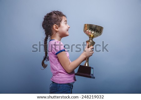 girl child six years of European appearance holds a cup in his hands, happiness,  reward and joy on a gray background
