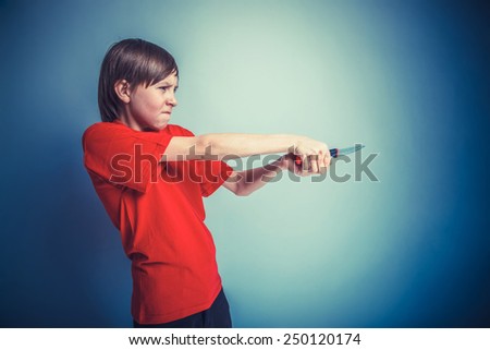 cross process European-looking boy of twelve years with a knife in his hand, his anger on a gray background