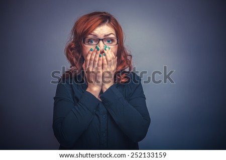 European-looking woman of thirty  years  covers  mouth with  her  hands,  surprised on a gray background retro
