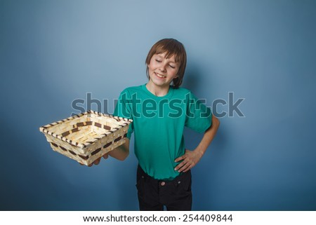 boy teenager European appearance brown hair in a shirt holding a wicker box outstretched hands on a gray background, smiling