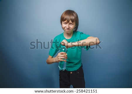 boy teenager European appearance in a green T-shirt can not open a bottle on a gray background, sadness, resentment