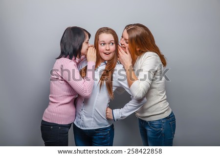 two girls European appearance blonde and brunette whispered in his ear the secret third blonde girl on a gray background