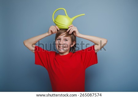 boy teenager European appearance in a red shirt brown hair watering can put on his head sticking her hands on a gray background, joy