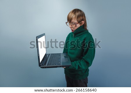 European-looking boy of ten years in glasses, it is worth looking at a laptop on a gray  background