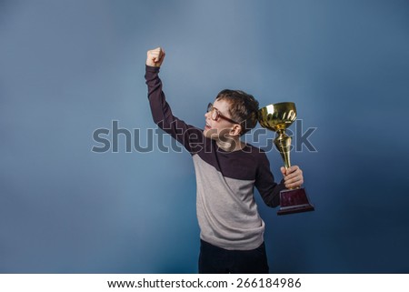 European-looking boy of ten years  in glasses  holding  a cup  in  his  hand,  pride, the reward on a  gray  background