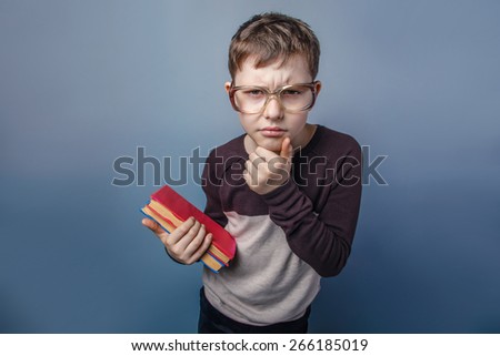 European-looking boy of ten years in glasses  holding  a book in his hands, unhappy on a gray background