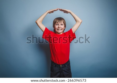 teenager boy brown European appearance in a red shirt folded his hands in the form of a roof over his head on a gray background, smile