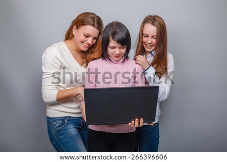 Three girls looking European appearance in computer laughing on a gray background, friendship, joy