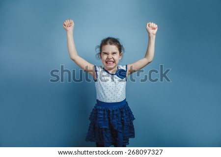 Teen girl of European appearance five years is angry hands up showing teeth on a gray background