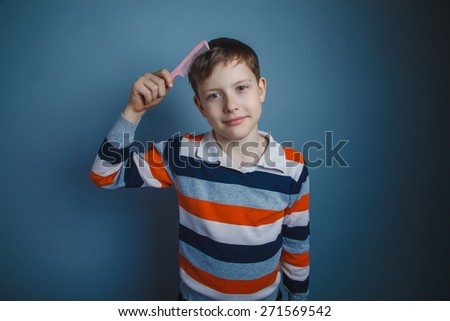 teenager boy of about ten European appearance brown hair combs her hair pink comb on a gray background, smile, care