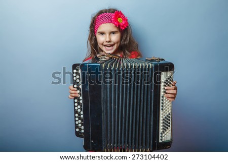girl seven years of European appearance with a bright-haired child playing on a hairpin akardeone on a gray background, music, song
