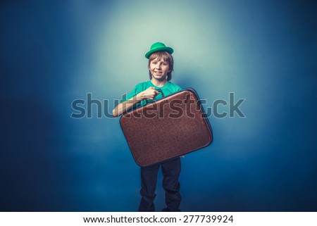 European-looking boy of  ten years in a hat holding a suitcase in hand, itinerary on a blue background instagram effect style
