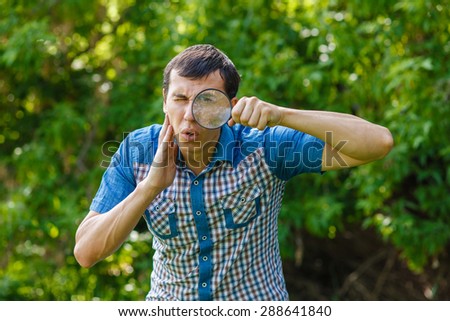 The man in the street holding a magnifying glass big eyes on a green  background  leaves  summer