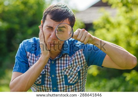 The man in the street holding a magnifying glass big eyes on a green background leaves  summer