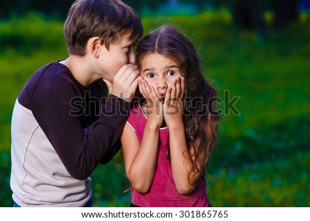 girl whispering in the ear of the boy tells the secret hearings in nature photos