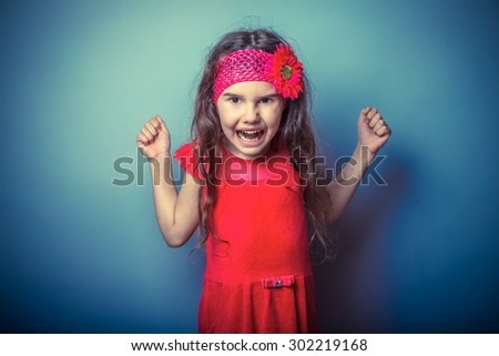 a girl of seven European appearance brunette in a bright dress clenched fists shouting on gray background, anger, rage, scream retro photo effect