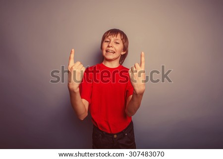 boy teenager European appearance in a red shirt shows the number two fingers on a gray background retro