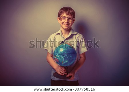 baby boy of ten European appearance in a light brown shirt and glasses holding a globe and smiling on a light background retro