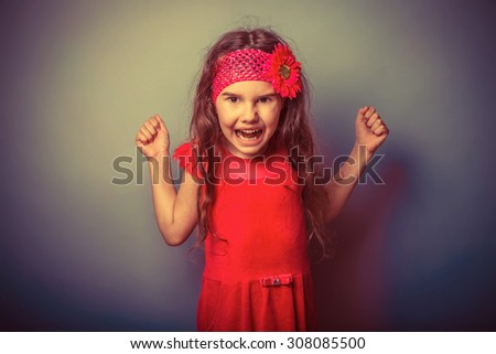 a girl of seven European appearance brunette in a bright dress clenched fists shouting on gray background, anger, rage, scream retro