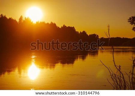 Evening sunset on the river sun sets orange light silhouettes the nature and trees reflected in water