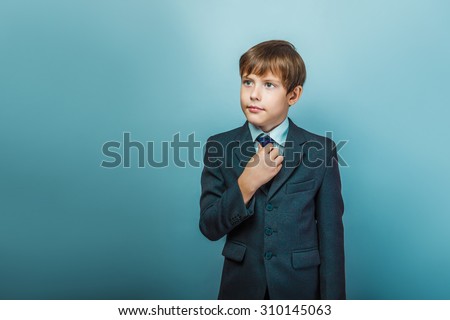 a boy of twelve European appearance in a suit straightens his tie on a gray background