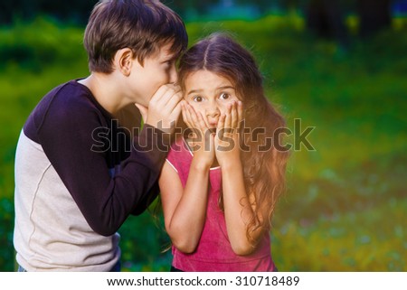 girl whispering in the ear of the boy tells the secret hearings in nature photos sunlight