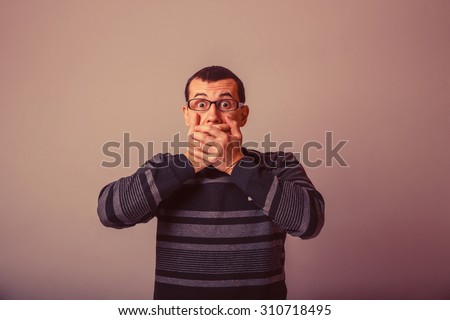 European-looking male of about thirty-closed mouth with her hands on a gray background, fear retro
