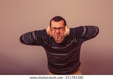 European-looking male of about thirty brunet covered his ears with his hands and closed his eyes on a gray background retro
