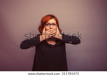 European appearance woman with glasses in a black shirt covering her mouth with her hands on a gray background, fright, fear retro
