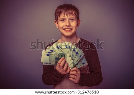 teenager boy Brown European appearance in brown jacket holding a wad of cash and smiling on a gray background, wealth, joy, bills retro