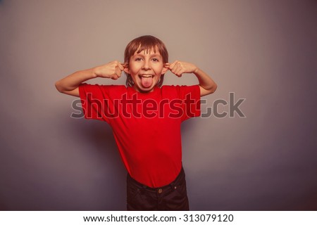 European-looking boy of ten years shows tongue, pulling the ears on gray background retro