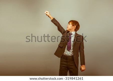 a boy of twelve European appearance in a suit holding his hands like Superman on a gray  background retro