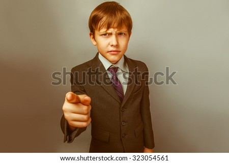 a boy of twelve European appearance in a suit shows a finger at the camera on a gray background retro