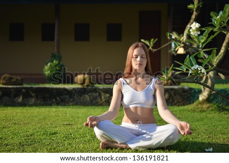 Yoga in white. Young woman sitting in a garden in yoga position.