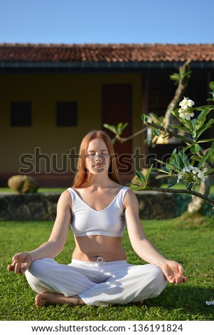 Yoga i white. Young woman sitting in a garden in yoga position.