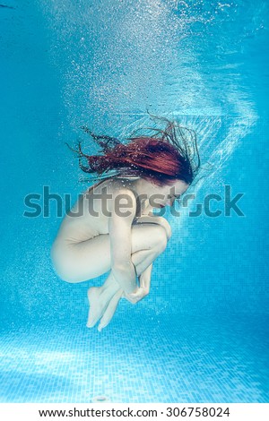 Young naked redhead woman underwater in a swimming pool