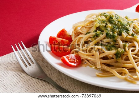Pasta with pesto sauce on a top with cherry tomato decoration on red background