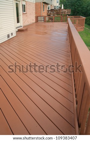 A freshly painted and stained wood deck with railing on a summer afternoon after a rain shower.