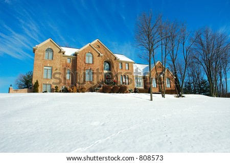 Two story brick American house sitting on a snow covered hill in winter under a brilliant deep blue sky.  Decorated for the Christmas holiday season.