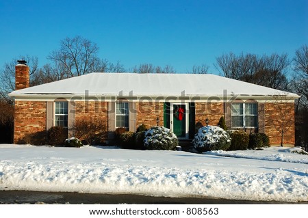 Single story brick American house sitting on a snow covered hill in winter under a brilliant deep blue sky.