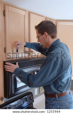 Man using a screwdriver to repair his microwave in the kitchen of a modern home.