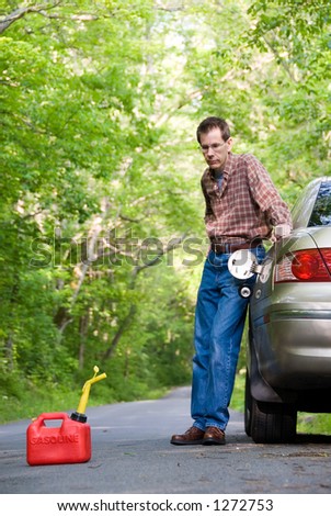 Upset man on a country road, staring at a gas can sitting  on the road next to his car.  Focus is on the gas can.