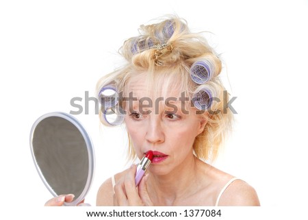 Curler Woman. A blonde woman with lavender curlers in her hair looks into her hand mirror and applies her lipstick.