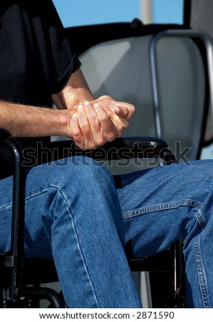 A man in a wheelchair sits with folded hands.